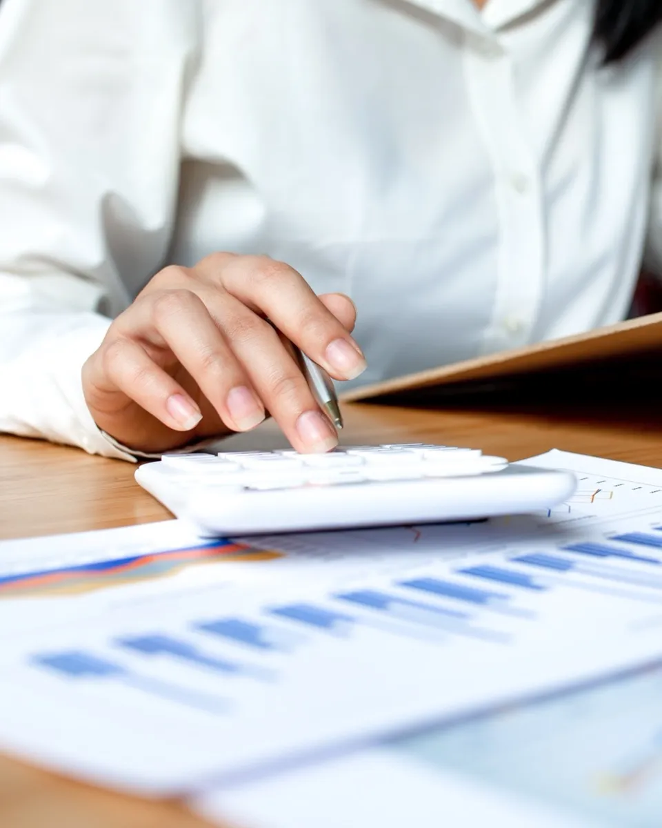 An accountant working through financial reports with a calculator and laptop